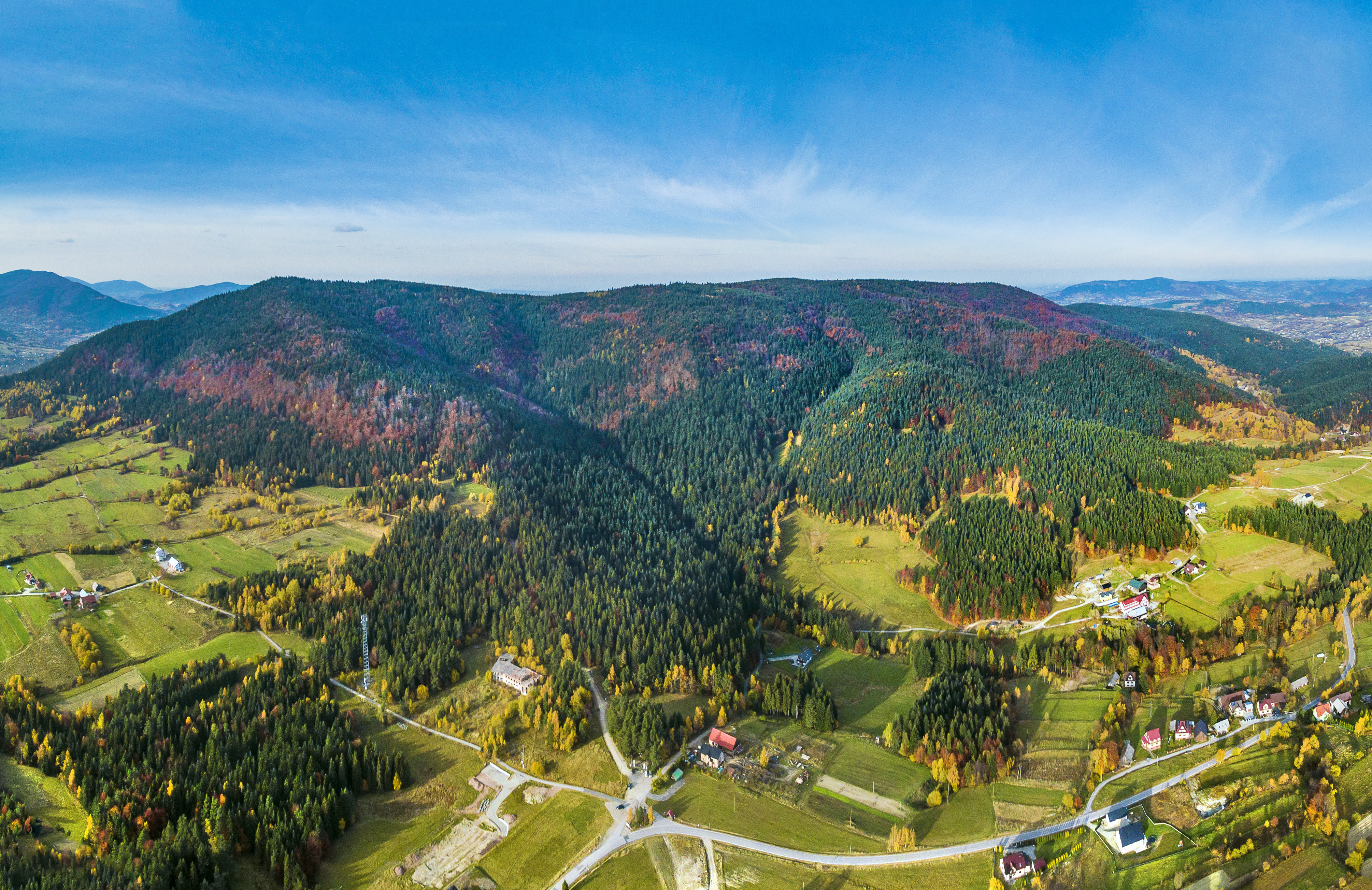 Widok z lotu ptaka na malownicze, zielone wzgórza i doliny w jesiennej kolorystyce.